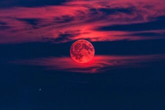 Deep red 'Blood Moon' during a total lunar eclipse, with visible stars in the dark night sky.