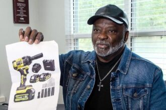 Sylvester Franklin, the victim of an AliExpress scam, holds up a low-resolution printed photo of a drill. The photo is in his hand, highlighting the discrepancy between the advertised product and the actual item received.